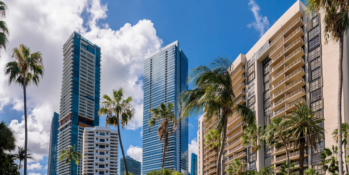 Tall condominium buildings surrounded by palm trees in front of a blue sky